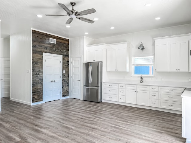 kitchen featuring white cabinets, stainless steel fridge, wood walls, and light hardwood / wood-style flooring