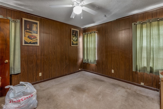 carpeted spare room featuring a textured ceiling, ceiling fan, and wooden walls