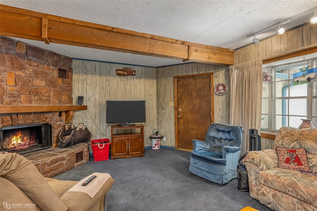 living room with dark carpet, track lighting, a stone fireplace, a textured ceiling, and beamed ceiling