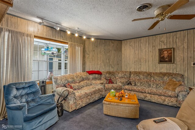 carpeted living room featuring a textured ceiling, ceiling fan, and wood walls