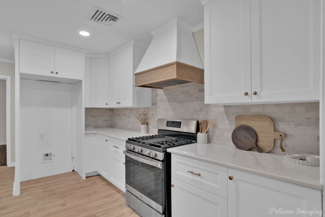 kitchen with tasteful backsplash, custom exhaust hood, white cabinetry, light hardwood / wood-style floors, and stainless steel range with gas cooktop