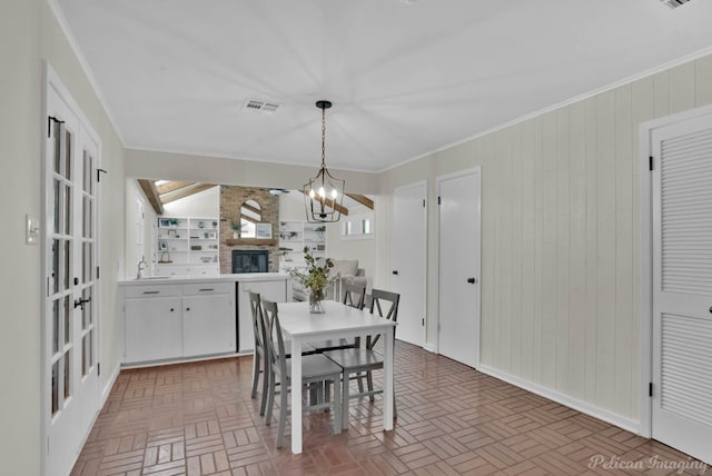 dining area with french doors, sink, a brick fireplace, ornamental molding, and a chandelier