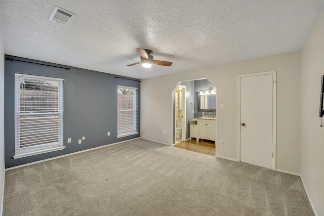 unfurnished bedroom with light carpet, connected bathroom, a textured ceiling, and ceiling fan