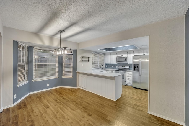 kitchen with pendant lighting, appliances with stainless steel finishes, backsplash, white cabinets, and kitchen peninsula