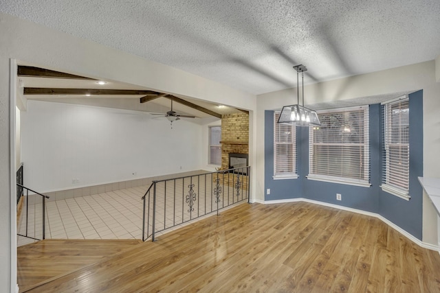 empty room with lofted ceiling with beams, ceiling fan, a fireplace, and light hardwood / wood-style floors