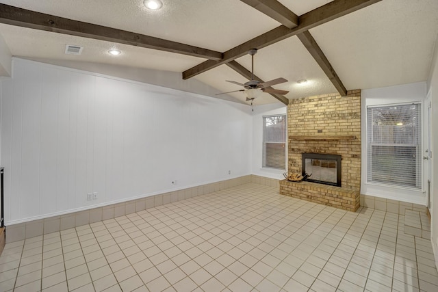 unfurnished living room with ceiling fan, vaulted ceiling with beams, a textured ceiling, light tile patterned flooring, and a brick fireplace