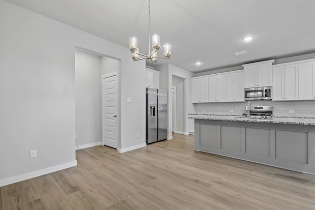 kitchen with light stone countertops, stainless steel appliances, tasteful backsplash, white cabinets, and light wood-type flooring