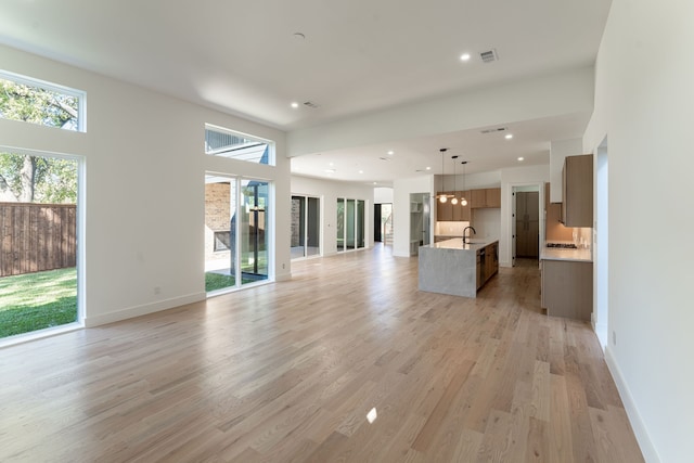 unfurnished living room with a towering ceiling, light wood-type flooring, and sink