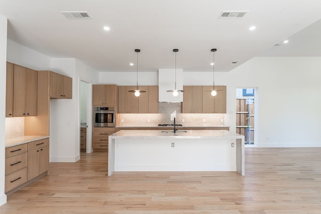 kitchen with light wood-type flooring, decorative light fixtures, a center island with sink, and stainless steel oven