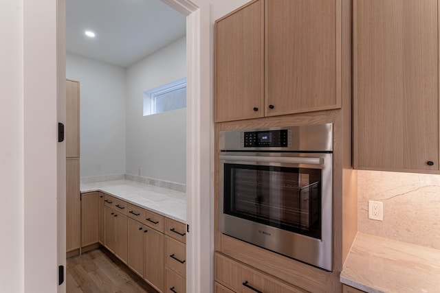 kitchen with light brown cabinets, light stone counters, backsplash, oven, and light wood-type flooring