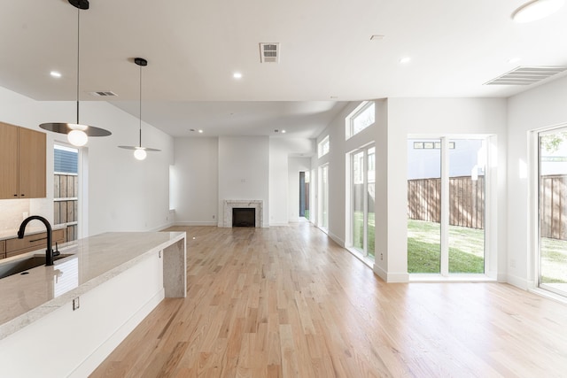 kitchen featuring plenty of natural light, light stone counters, decorative light fixtures, and light hardwood / wood-style flooring