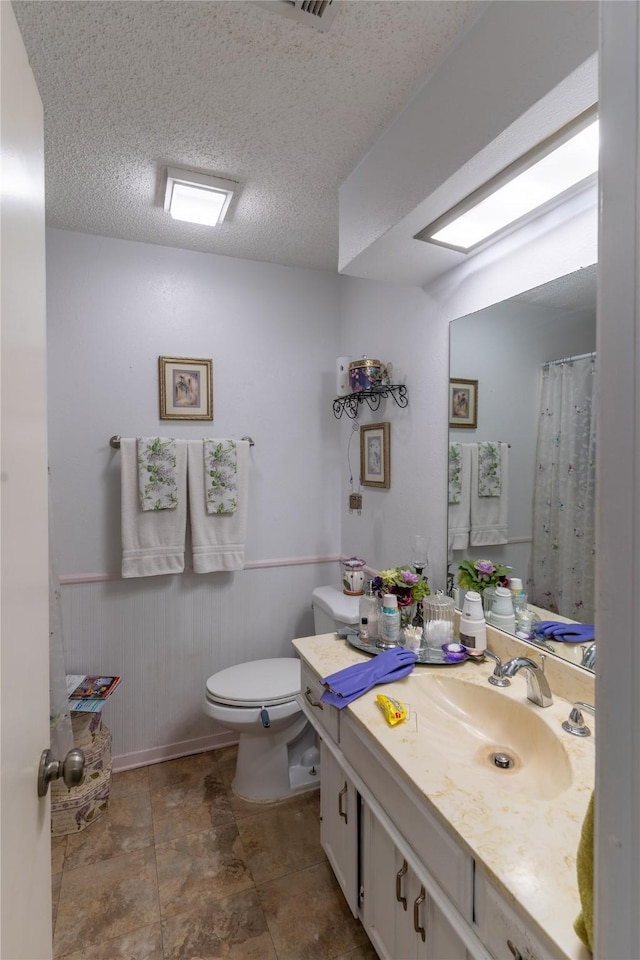 bathroom featuring wooden walls, vanity, a textured ceiling, and toilet