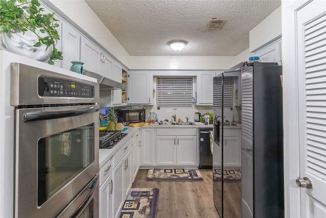 kitchen with a textured ceiling, stainless steel appliances, sink, wood-type flooring, and white cabinetry