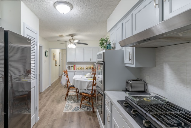 kitchen featuring ceiling fan, range hood, black gas stovetop, light hardwood / wood-style floors, and white cabinets