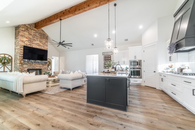 kitchen with white cabinetry, hanging light fixtures, stainless steel appliances, a center island with sink, and light wood-type flooring