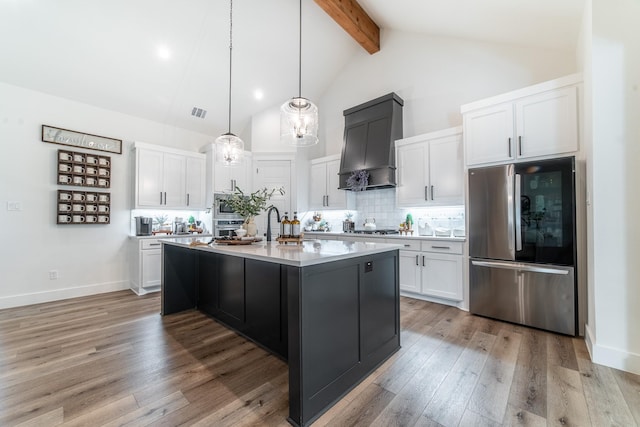 kitchen with white cabinets, appliances with stainless steel finishes, premium range hood, and an island with sink