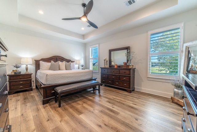 bedroom featuring ceiling fan, a raised ceiling, and light hardwood / wood-style flooring