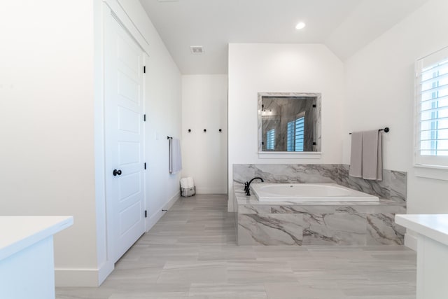 bathroom with vanity, lofted ceiling, and tiled tub