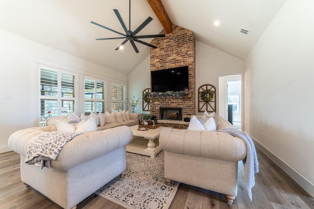 living room with ceiling fan, beamed ceiling, high vaulted ceiling, hardwood / wood-style floors, and a fireplace