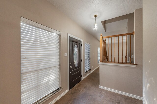 entryway featuring dark tile patterned flooring, lofted ceiling, and a textured ceiling