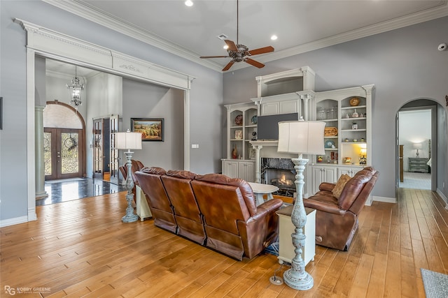 living room with french doors, ornamental molding, ceiling fan with notable chandelier, light hardwood / wood-style flooring, and a premium fireplace