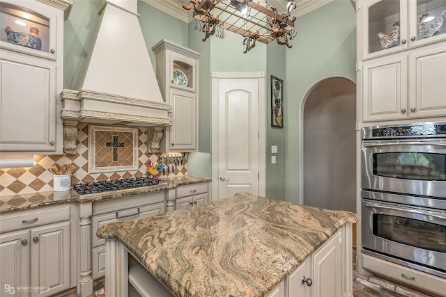 kitchen with light stone counters, a kitchen island, stainless steel appliances, and custom exhaust hood