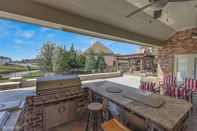 view of patio / terrace featuring ceiling fan, exterior kitchen, a pergola, area for grilling, and a water view