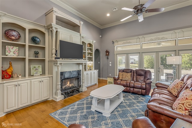 living room featuring ceiling fan, light hardwood / wood-style flooring, a high end fireplace, and ornamental molding