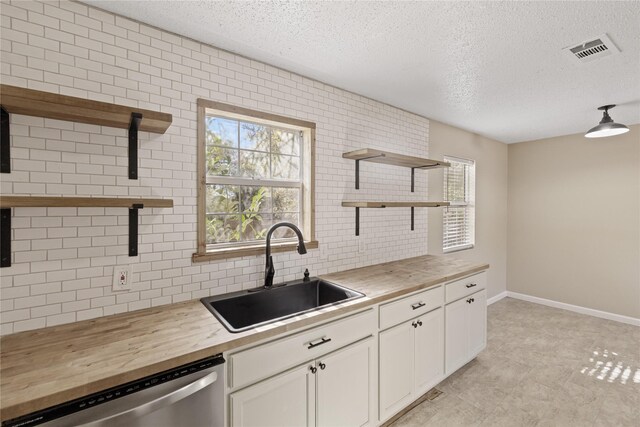 kitchen featuring sink, white cabinets, stainless steel dishwasher, and wood counters