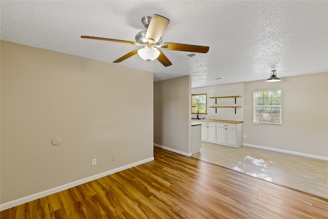 unfurnished living room with ceiling fan, sink, a textured ceiling, and light wood-type flooring