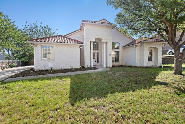mediterranean / spanish house featuring fence, a front yard, brick siding, and a tile roof