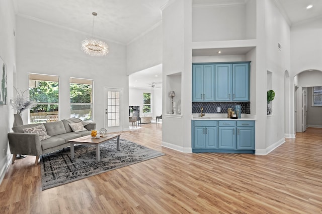 living room featuring a high ceiling, crown molding, arched walkways, and light wood-type flooring