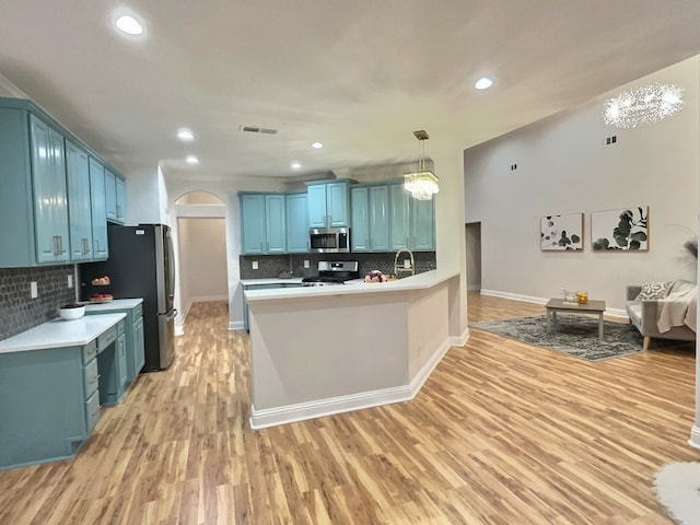 kitchen with kitchen peninsula, appliances with stainless steel finishes, light wood-type flooring, tasteful backsplash, and a chandelier