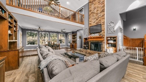 living room with a stone fireplace, ceiling fan, a towering ceiling, and light hardwood / wood-style floors