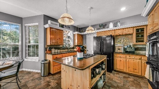 kitchen featuring pendant lighting, black appliances, decorative backsplash, a textured ceiling, and a kitchen island