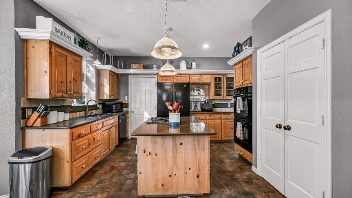 kitchen with backsplash, black appliances, sink, decorative light fixtures, and a kitchen island