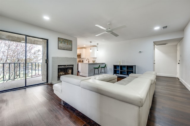 living room with sink, ceiling fan, a stone fireplace, and dark wood-type flooring