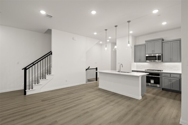 kitchen featuring sink, gray cabinets, an island with sink, dark hardwood / wood-style flooring, and stainless steel appliances