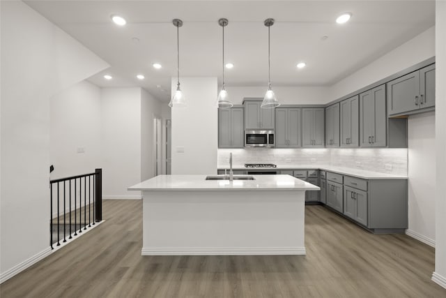 kitchen featuring hardwood / wood-style flooring, decorative light fixtures, sink, and a kitchen island with sink