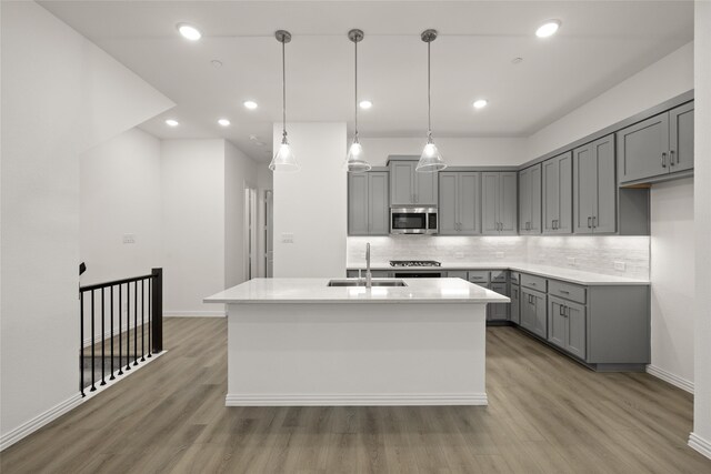 kitchen featuring hardwood / wood-style flooring, decorative light fixtures, sink, and a kitchen island with sink