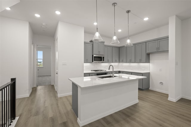 kitchen featuring sink, stainless steel appliances, light hardwood / wood-style flooring, pendant lighting, and a center island with sink