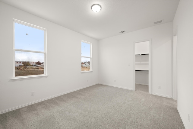 unfurnished bedroom with light carpet, a spacious closet, and a closet