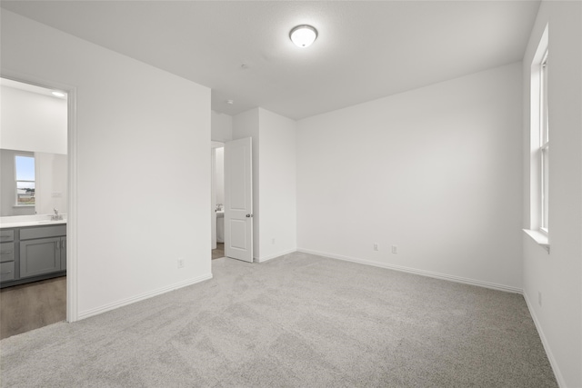 unfurnished bedroom featuring light colored carpet, sink, and ensuite bath