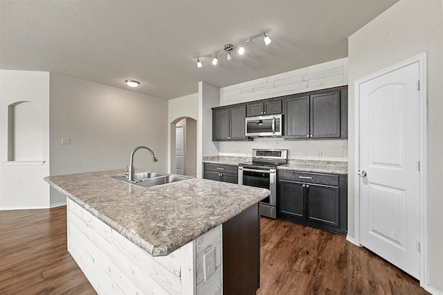 kitchen with dark wood-type flooring, a kitchen island with sink, sink, and stainless steel appliances