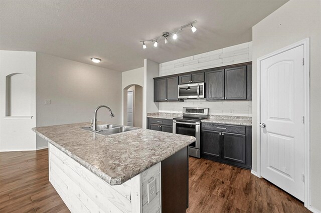 kitchen with dark wood-type flooring, a kitchen island with sink, sink, and stainless steel appliances