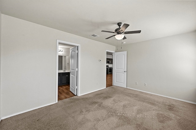 unfurnished bedroom featuring ceiling fan, ensuite bathroom, and dark colored carpet