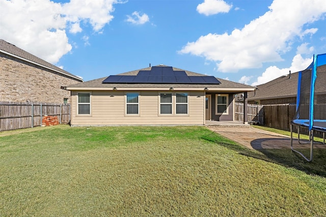 rear view of property featuring a lawn, solar panels, and a trampoline