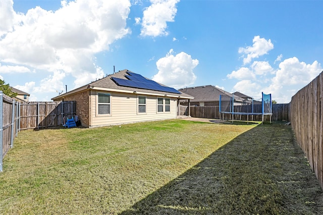 back of house with a lawn, solar panels, and a trampoline