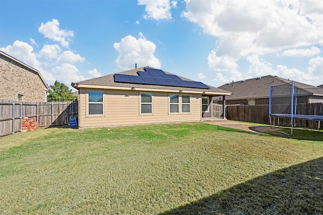 back of property featuring solar panels, a yard, and a trampoline