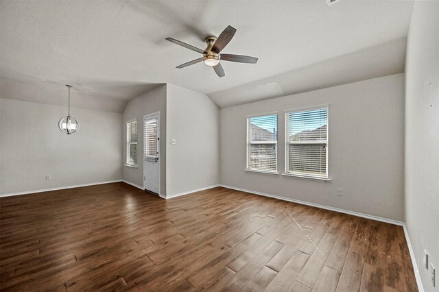 spare room with ceiling fan with notable chandelier, dark hardwood / wood-style floors, and vaulted ceiling